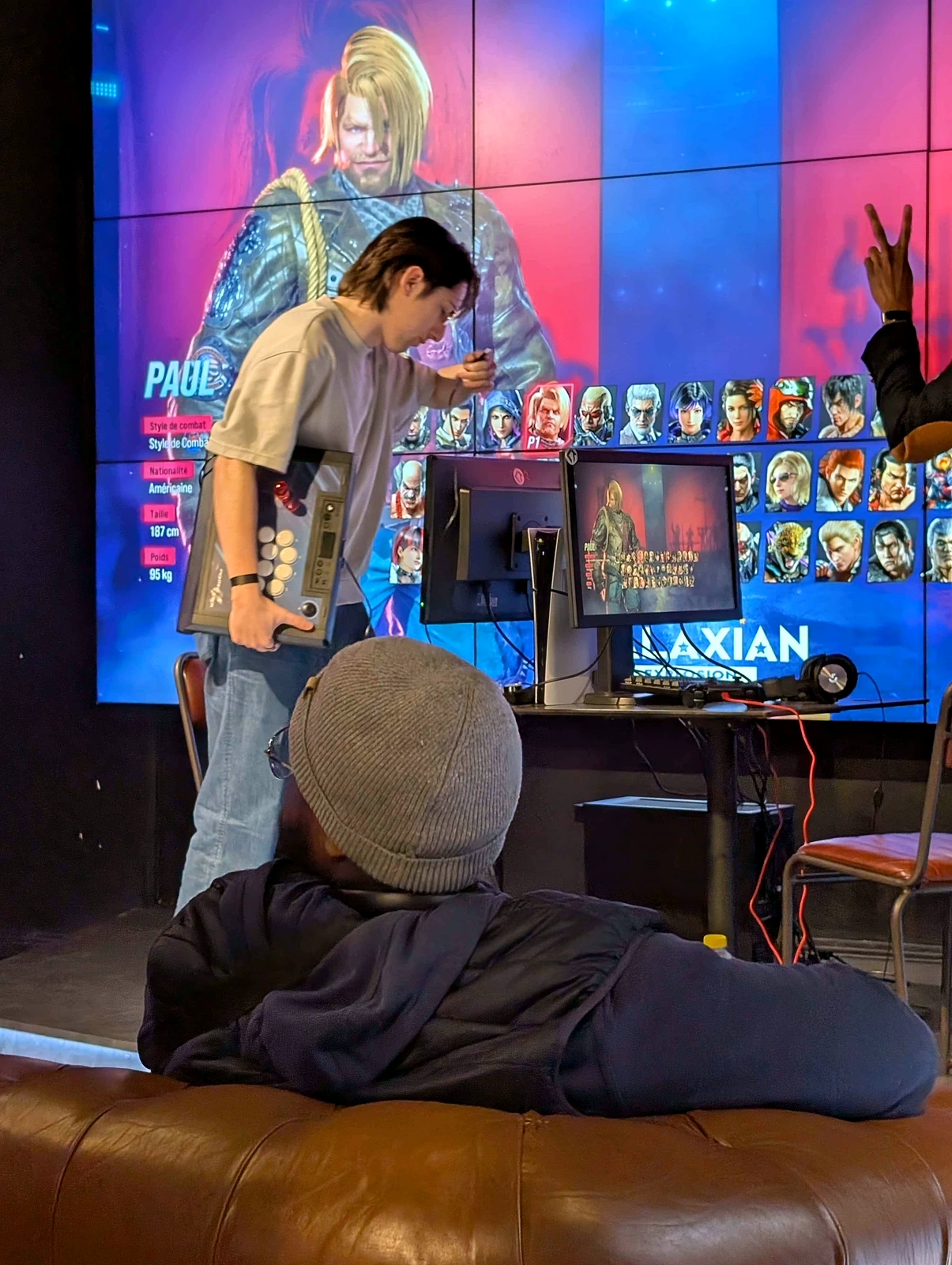 Compétiteur Claws avec son stick devant l'écran de sélection Tekken 8